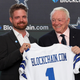 Blockchain.com CEO Peter Smith holds a jersey emblazoned with the number 1 and "Blockchain.com" alongside Dallas Cowboys owner Jerry Jones, both smiling.